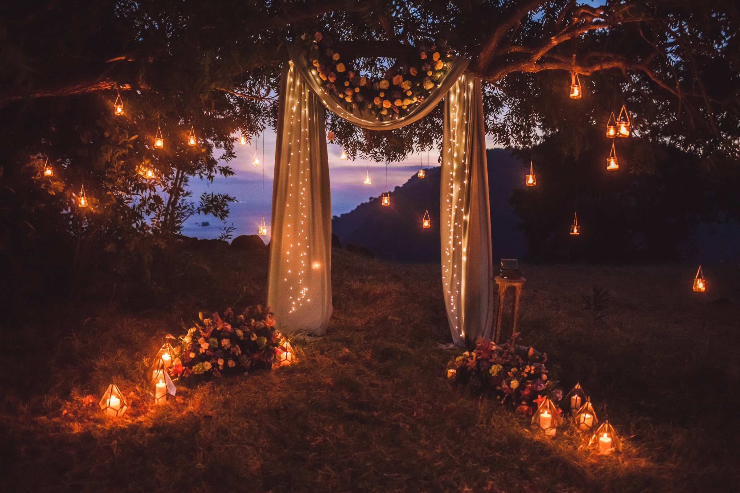 Draped floral arch with hanging candle lanterns at dusk