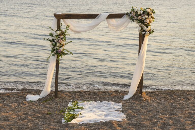 Wooden arch with white drapes and flowers by the sea