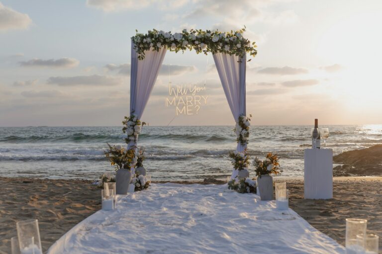 White draped proposal arch with flowers on a beach